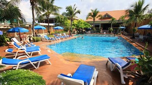 A swimming pool with blue lounge chairs and umbrellas, surrounded by palm trees and a building with a red roof. - Twin Palms Resort (Pattaya)