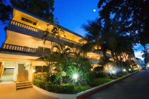 A multi-story hotel with a balcony, surrounded by palm trees and well-lit pathways.