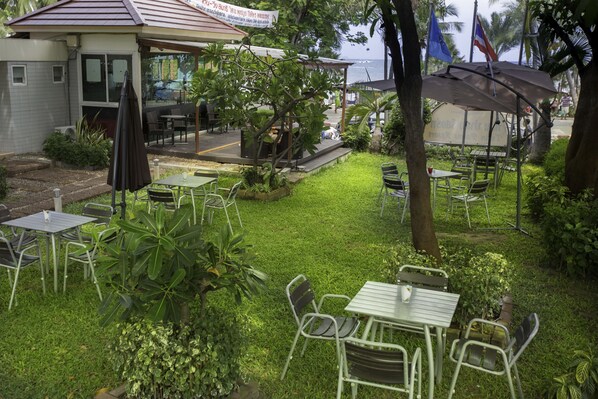 An outdoor seating area with tables and chairs, surrounded by greenery and a building with a sign.
