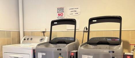 A laundry facility with dryers and washing machines, a sign indicating no shoes, and a fan on the wall.