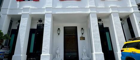 Un bâtiment blanc avec des volets rouges, une entrée centrale et deux statues de chaque côté.