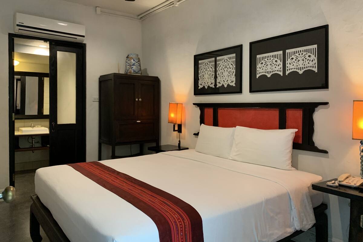 Une chambre d’hôtel comprenant un lit, une armoire, une table de chevet avec une lampe et deux panneaux décoratifs fixés au mur.