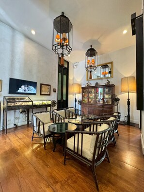 A room with a wooden floor, a dining table with chairs, a television, a cabinet with glass doors, and two hanging light fixtures. - 99 The Gallery Hotel (Chiang Mai)