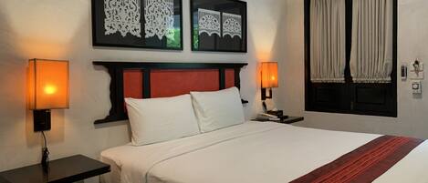 A hotel room with a bed, two bedside tables, a wall-mounted air conditioning unit, and a window with curtains.