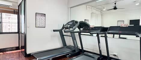 Un gimnasio con cintas de correr, ventilador de techo y piso de madera.
