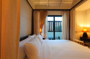 A hotel room with a large bed, two bedside lamps, a small table, and a view of the outdoors.