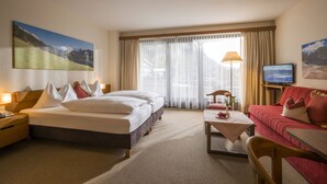 A hotel room with a bed, a sofa, a TV, and a painting of a mountain landscape. - Aparthotel Andreas Hofer (Kufstein)