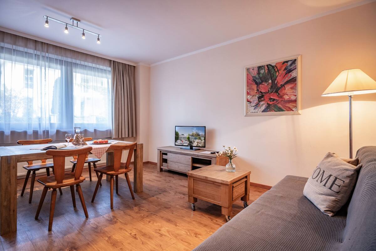 A modern living room with a dining area, wooden furniture, a flat-screen TV, and a painting on the wall.
