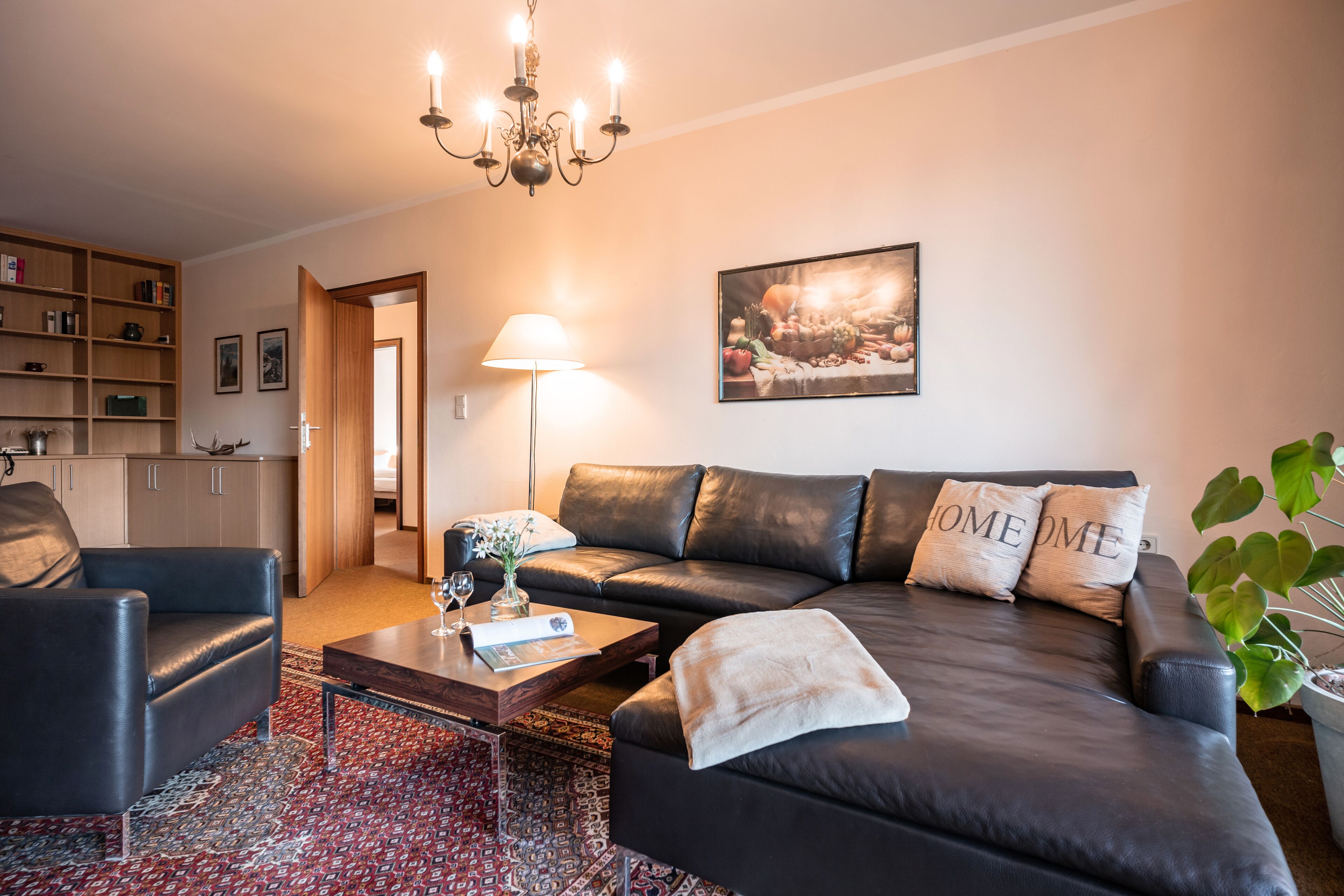 A modern living room with a black leather sofa, a wooden coffee table, and a patterned rug.
