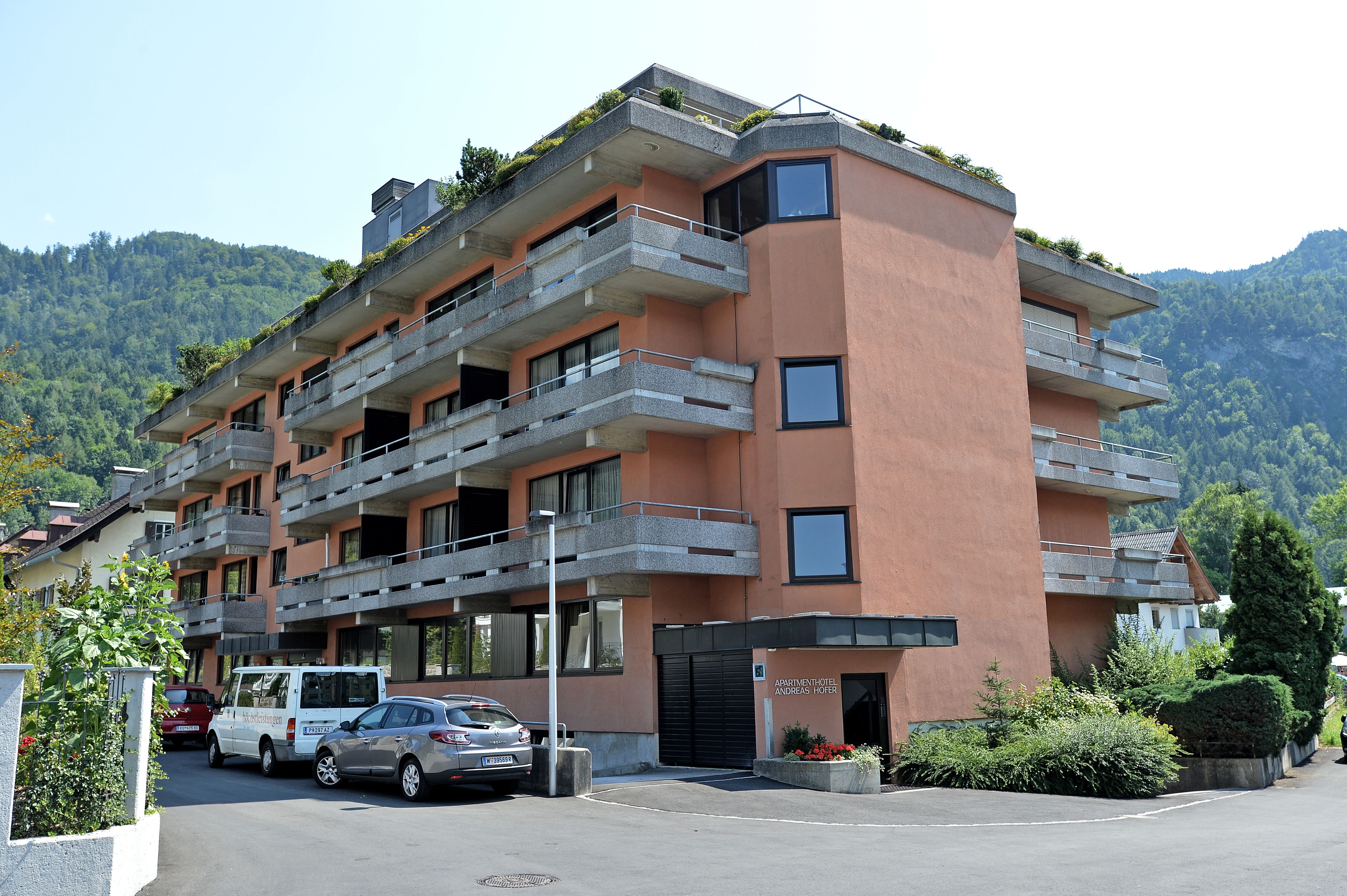 Un edificio a più piani con balconi, un'area di parcheggio e montagne sullo sfondo.