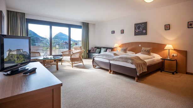 A hotel room with a bed, a desk with a TV, a chair, and a view of mountains. - Aparthotel Andreas Hofer (Kufstein)