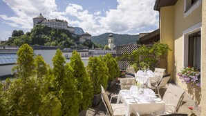 An outdoor dining area with tables and chairs, overlooking a castle and mountains. - Aparthotel Andreas Hofer (Kufstein)