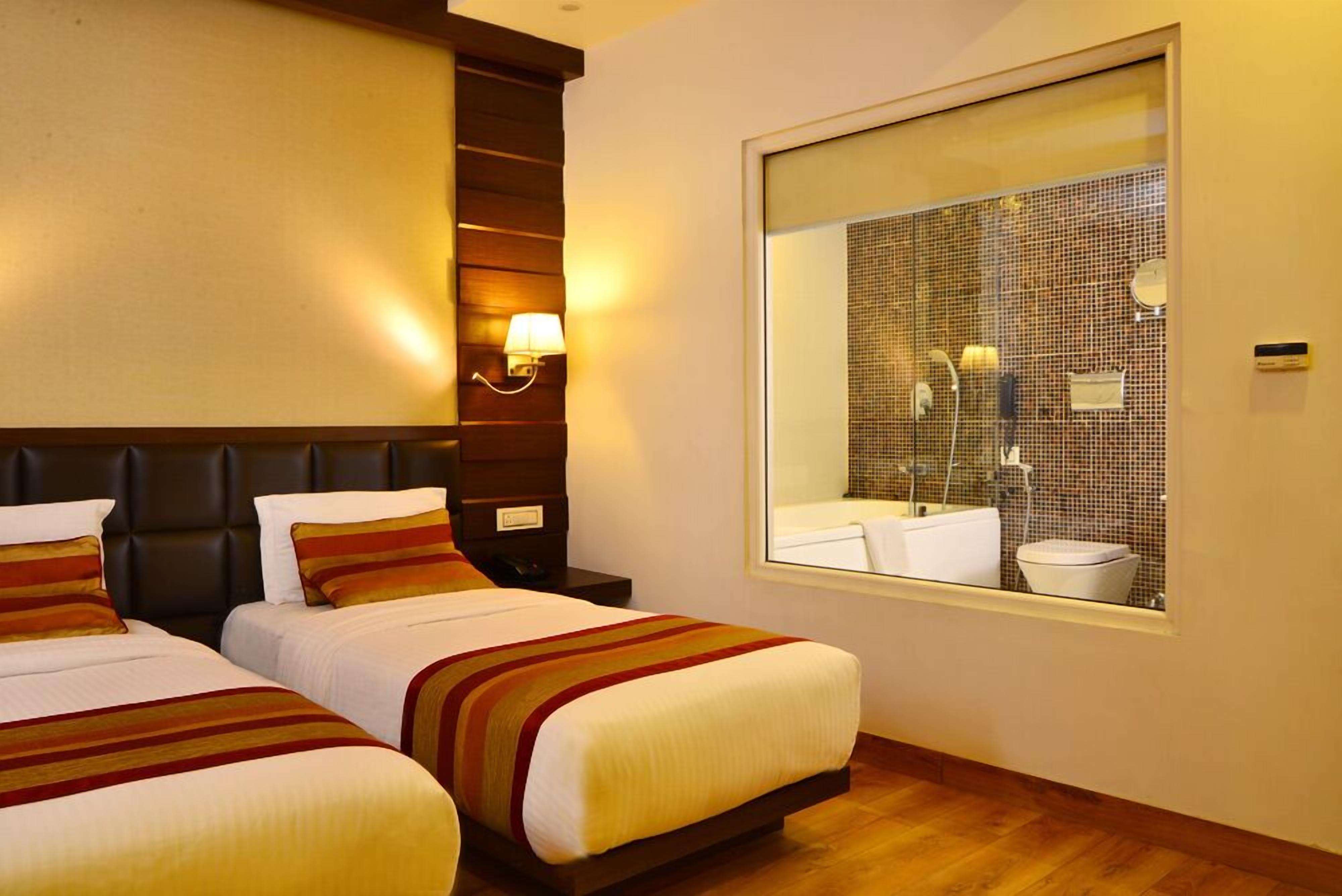 A hotel room with two beds, a large mirror, and a view of the bathroom.