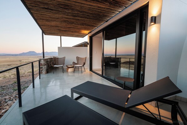 A modern outdoor seating area with lounge chairs and wicker chairs, overlooking a desert landscape. - Rostock Ritz Desert Lodge (Solitaire)