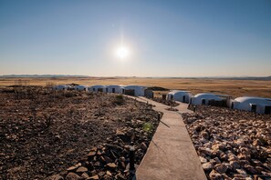 A desert landscape with a row of white dome-shaped structures, a concrete pathway, and distant mountains under a clear sky. - Rostock Ritz Desert Lodge (Solitaire)