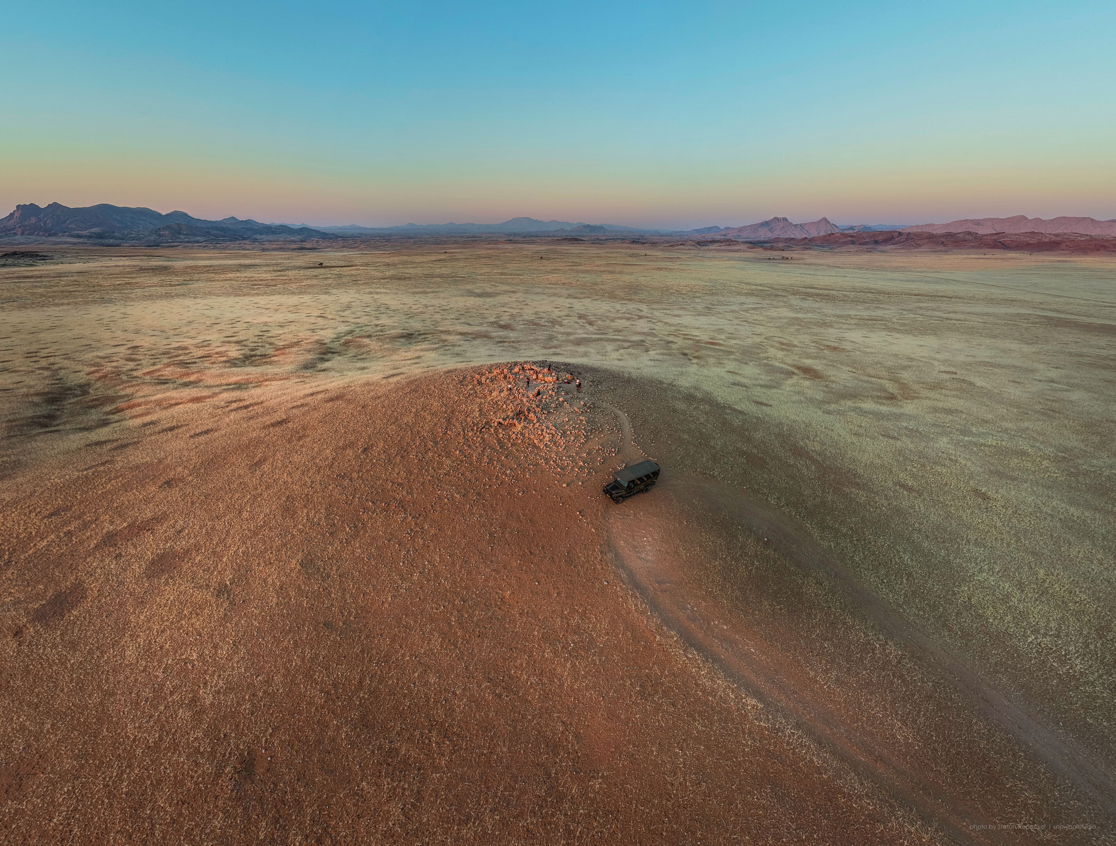 Vista aérea de un paisaje desértico con un vehículo estacionado cerca de un montículo de rocas.
