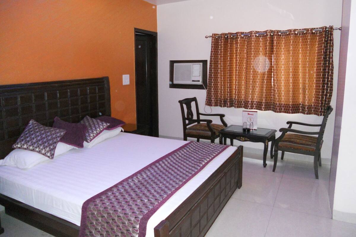 A hotel room with a bed, two chairs, a small table, and a window with curtains.
