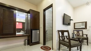 Habitació d'hotel amb una finestra gran, un televisor fixat a la paret, un frigorífic petit i dues cadires de fusta.