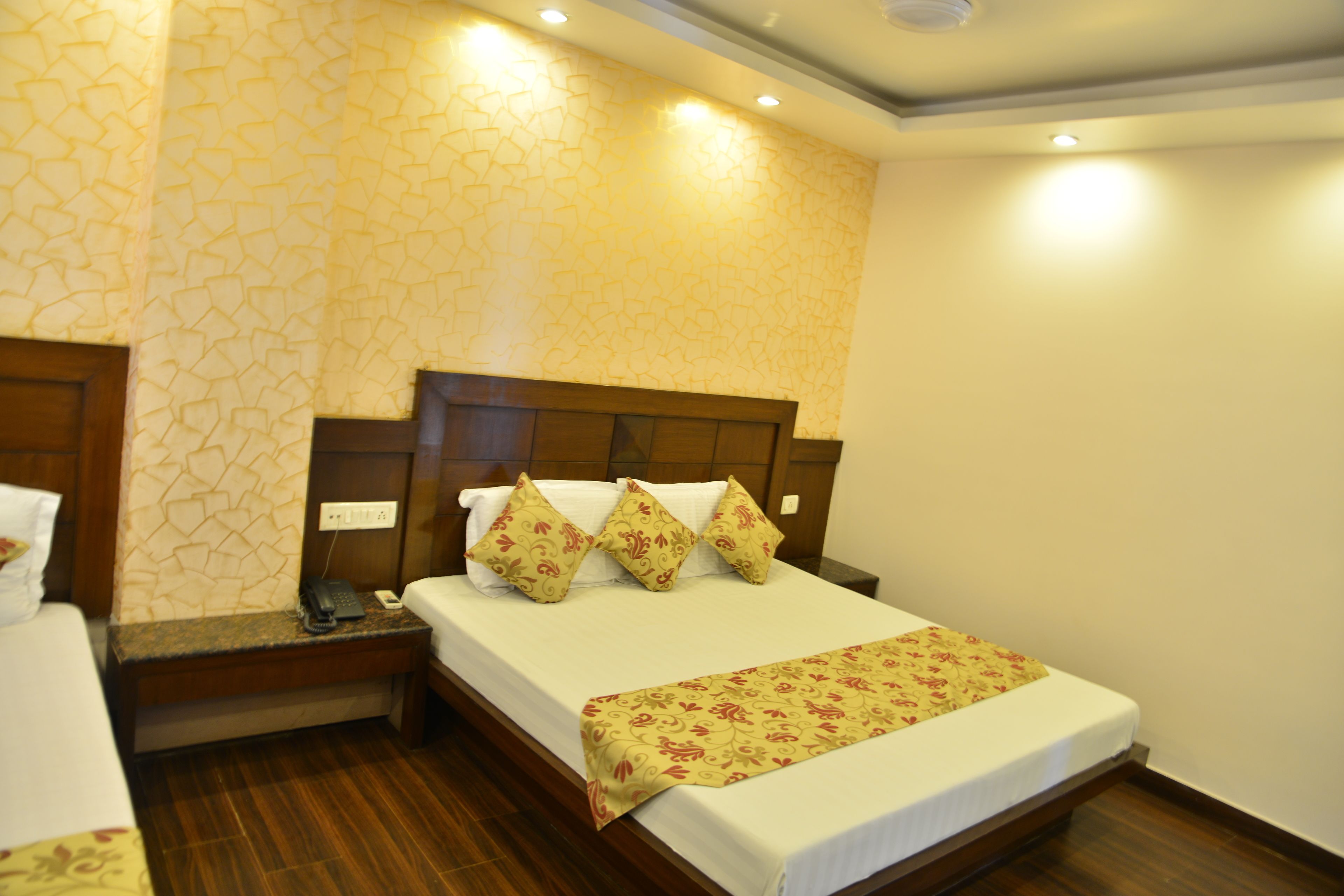 A hotel room with a bed, wooden headboard, bedside table, and a patterned wall.