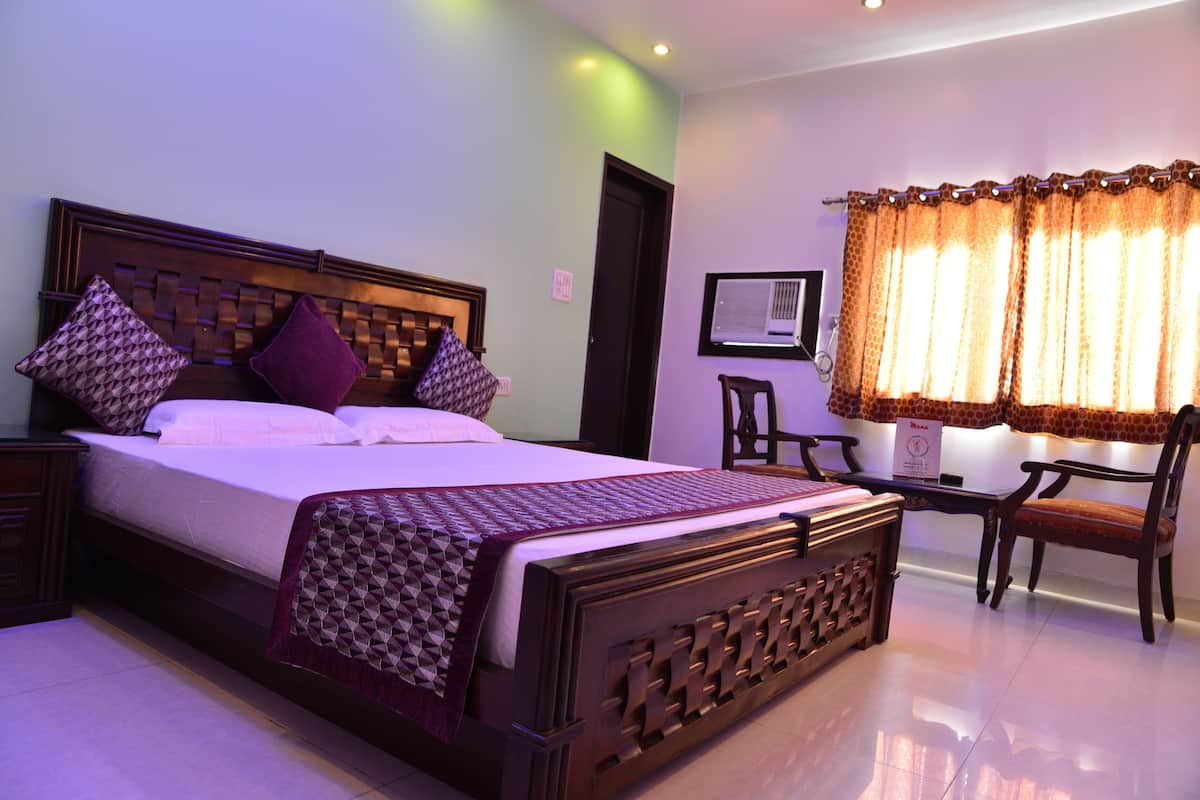 A neatly made bed with a patterned bedspread and pillows, a wooden headboard, and a bedside table with a lamp.