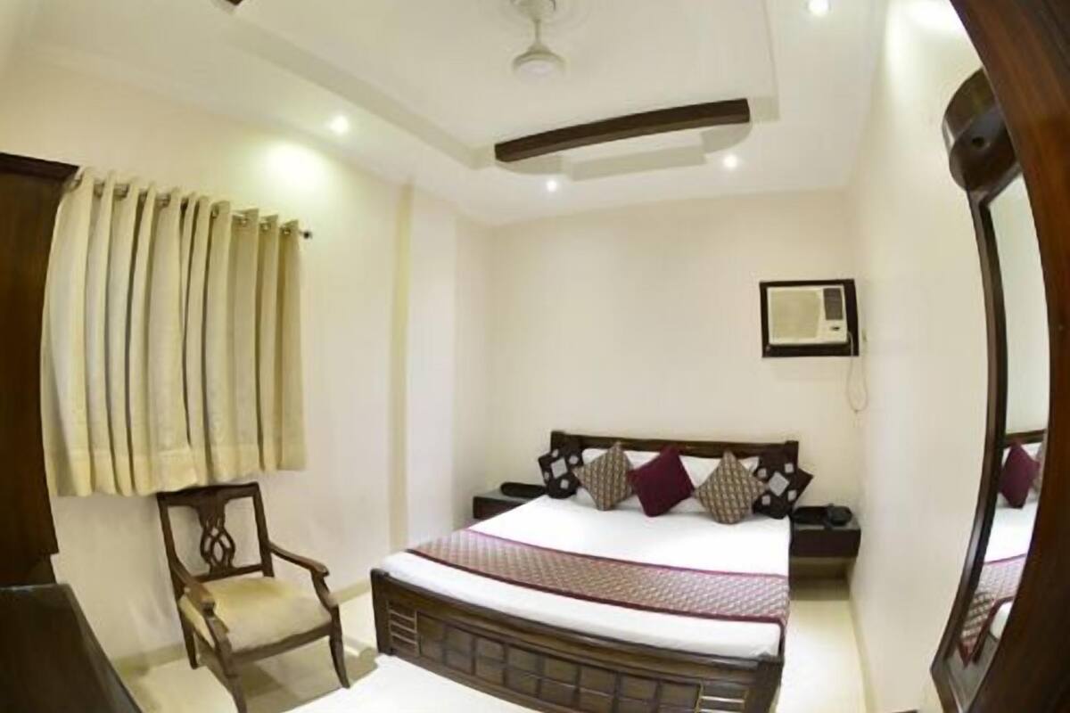 A hotel room with a bed, a chair, a ceiling fan, and a window with curtains.