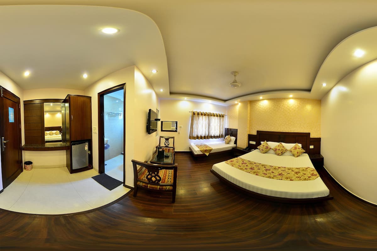 A hotel room with a curved ceiling, a bed with a floral bedspread, a small table with a chair, and a bathroom visible through an open door.