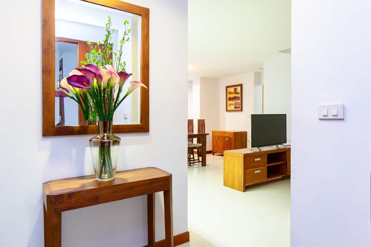 Una sala de estar con una consola de madera, un florero con flores, un televisor y un cuadro en la pared.