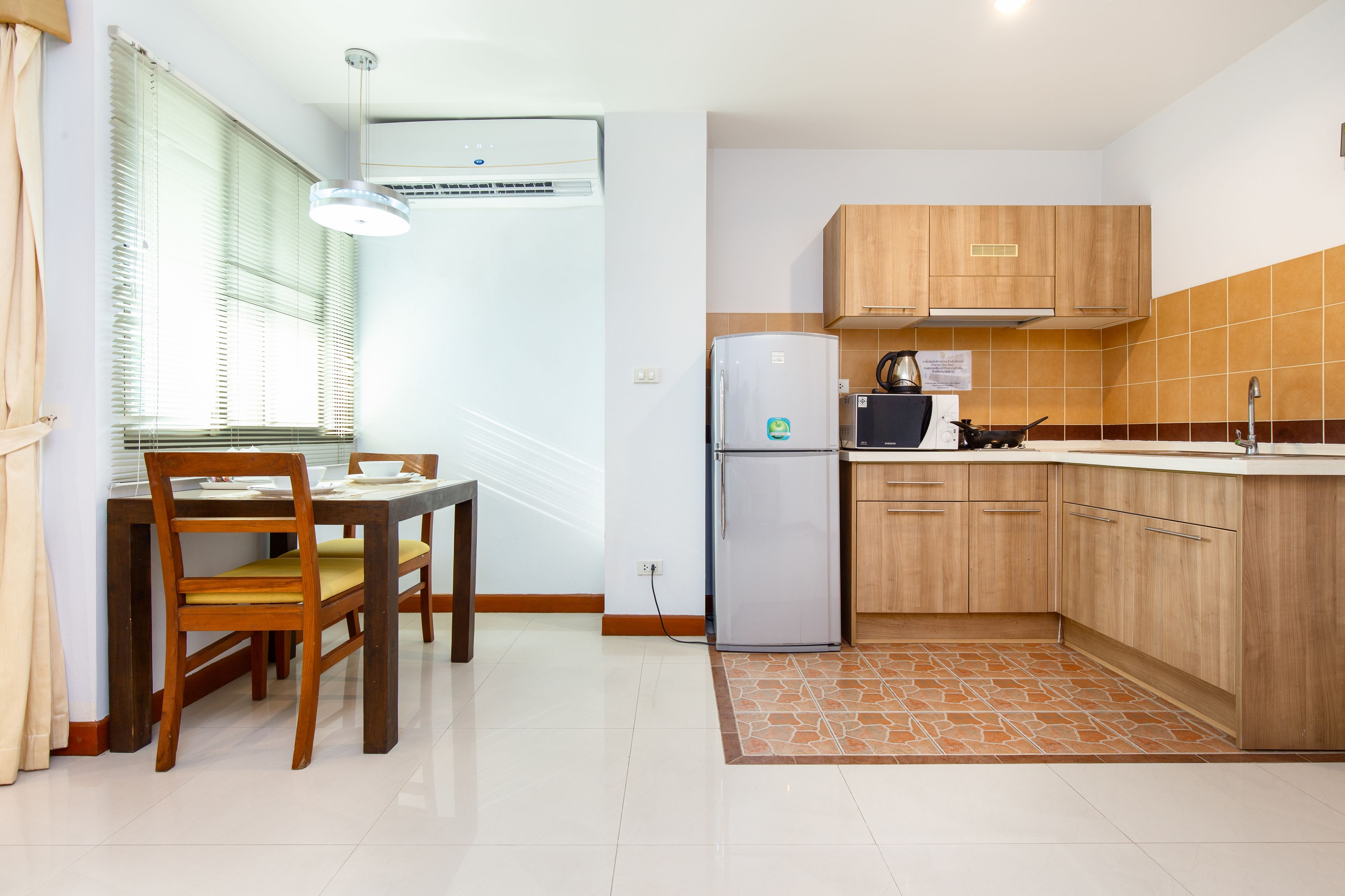 A compact kitchen with wooden cabinets, a refrigerator, and a dining area with a table and chairs.