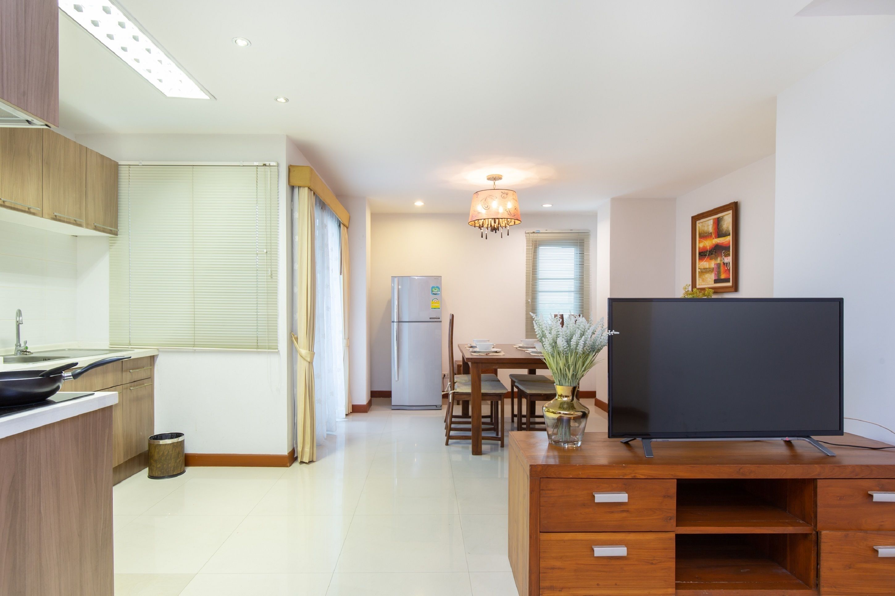 A modern kitchen with a dining area, a flat-screen TV, and a chandelier.