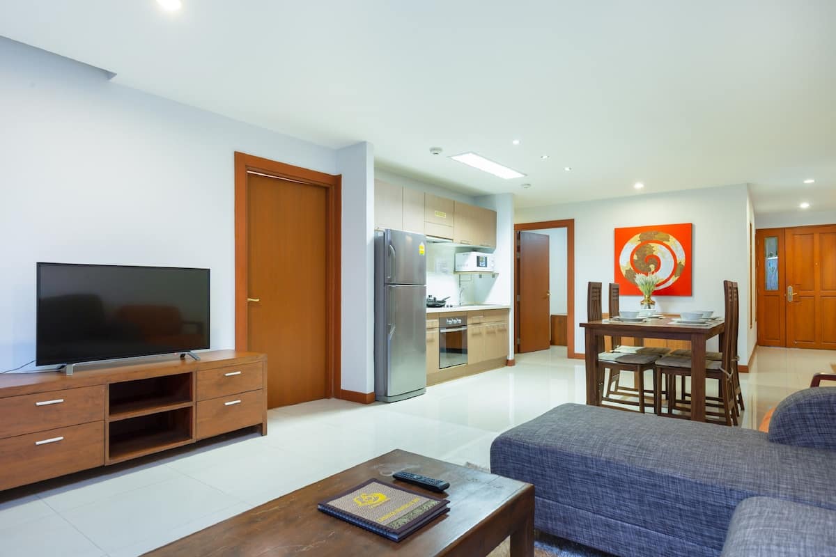 Una sala de estar moderna con un televisor de pantalla plana, un mueble de entretenimiento de madera y un sofá. Se ve, al fondo, un comedor con una mesa y sillas.