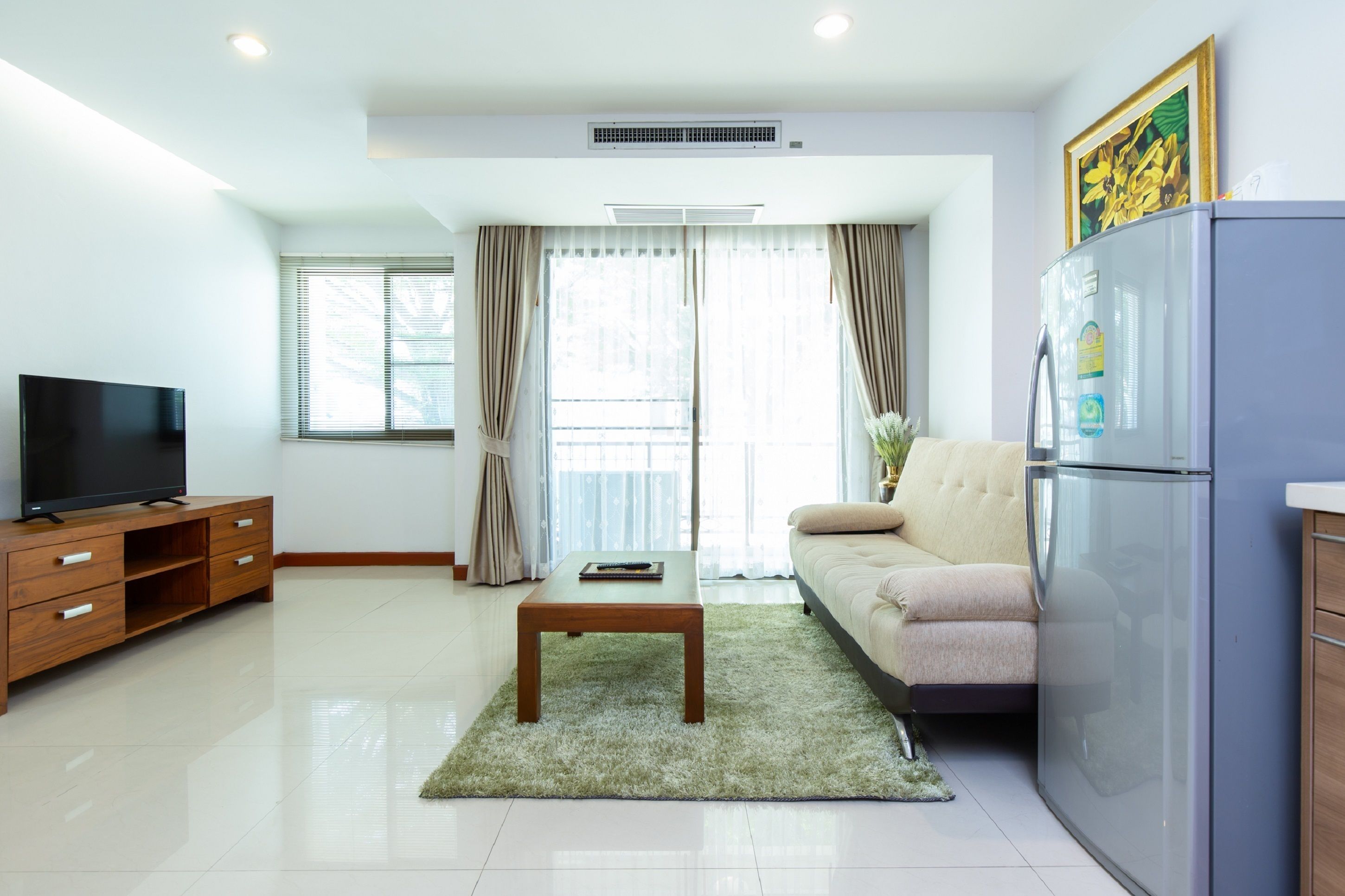 A modern living room with a flat-screen TV, a wooden coffee table, a sofa, and a refrigerator.