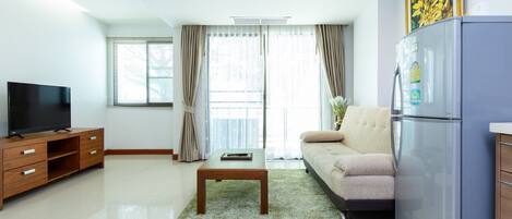 A modern living room with a flat-screen TV, a wooden coffee table, a sofa, and a refrigerator.