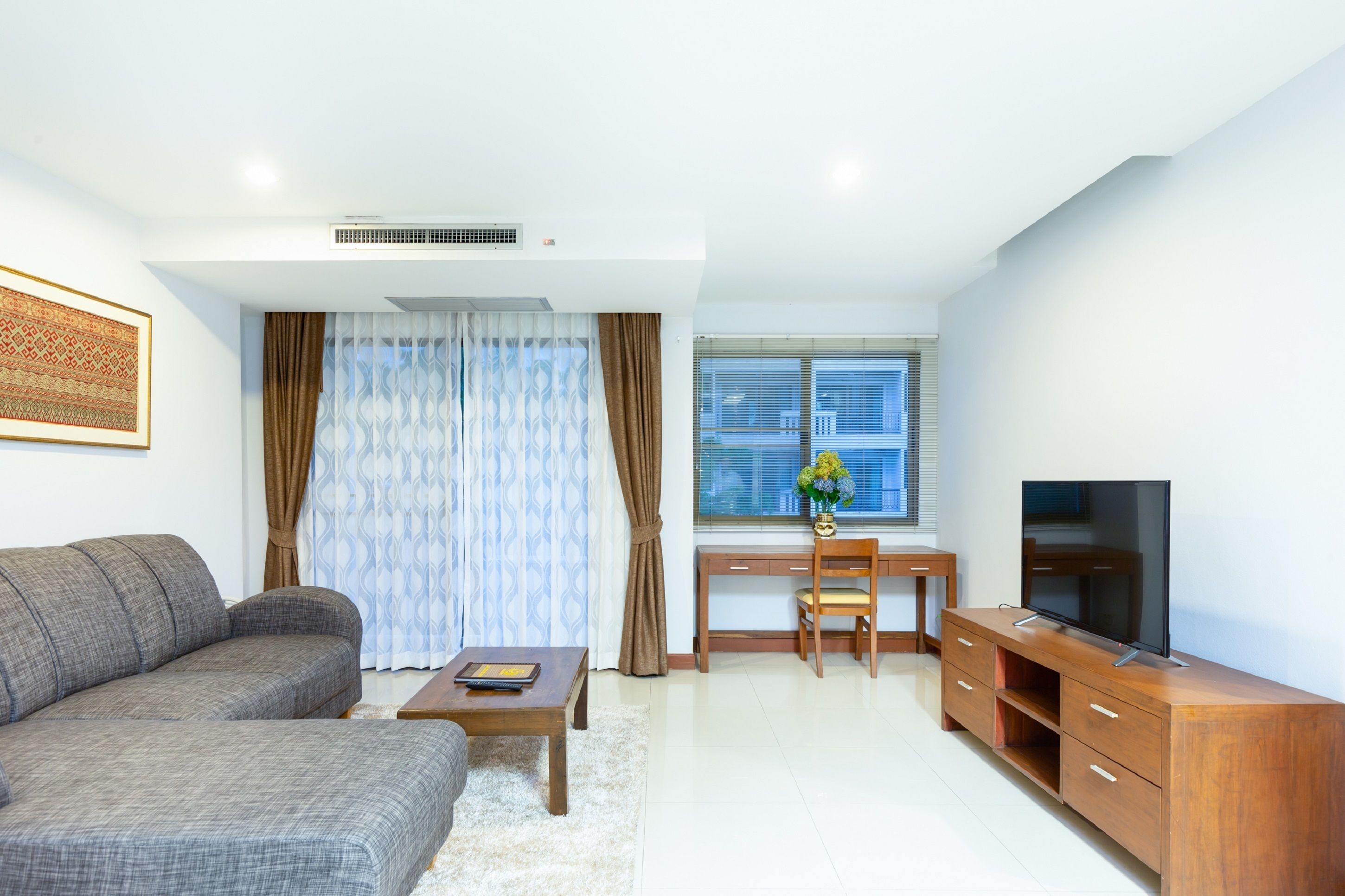 A modern living room with a sofa, coffee table, TV stand, and a desk with a chair.