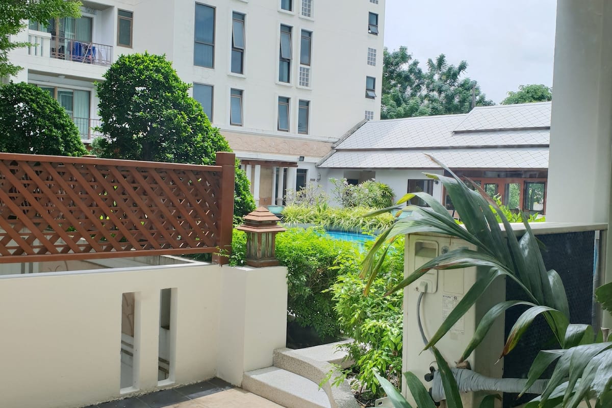 Un patio con piscina, rodeado de vegetación y un edificio de varios pisos con balcones.