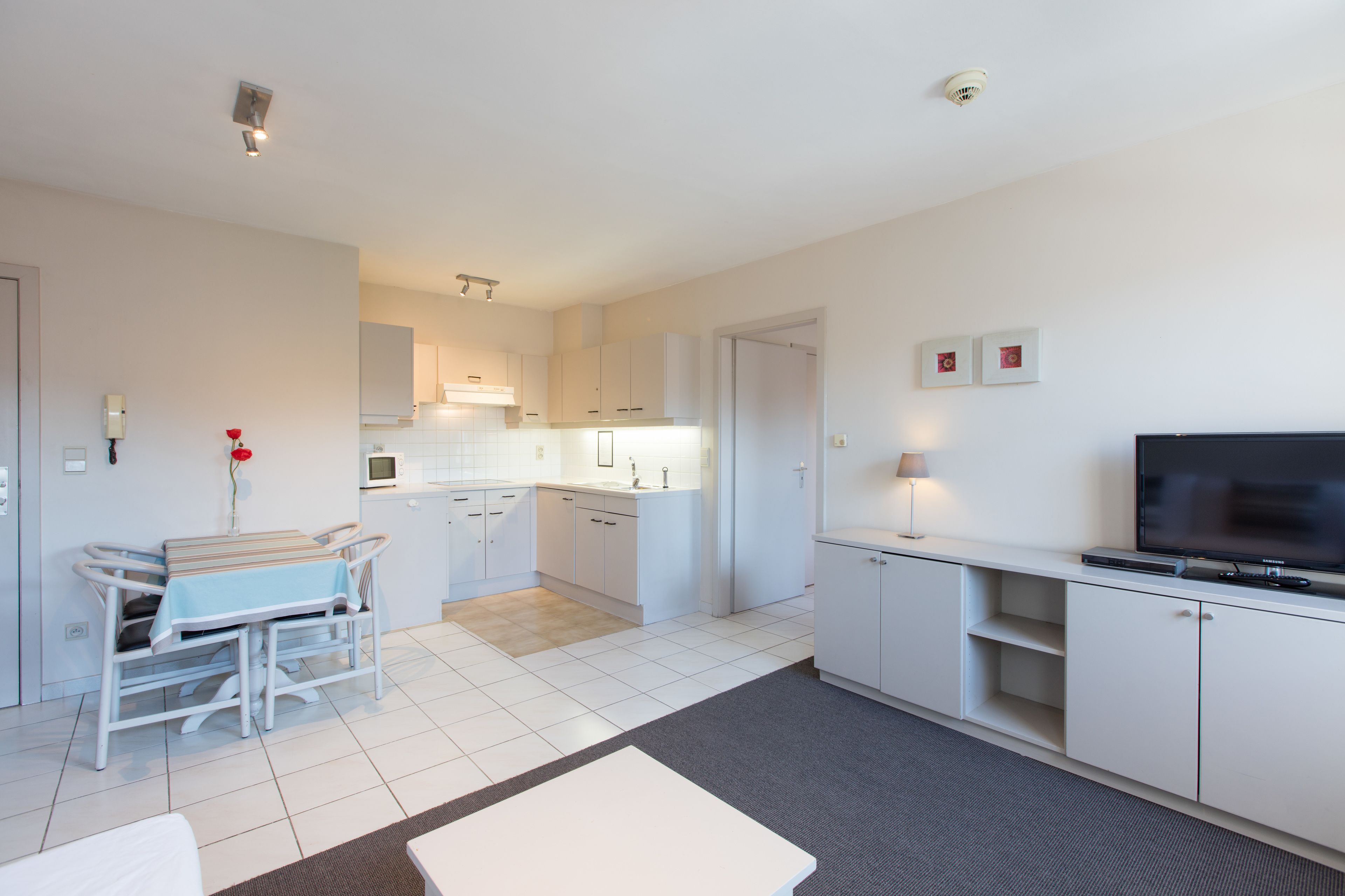 A modern kitchen with white cabinets, a dining area with a table and chairs, and a TV on a stand.