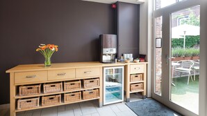 Ett modernt kök med en inbyggd kaffemaskin, ett kylskåp, korgar av rotting och en vas med blommor.
