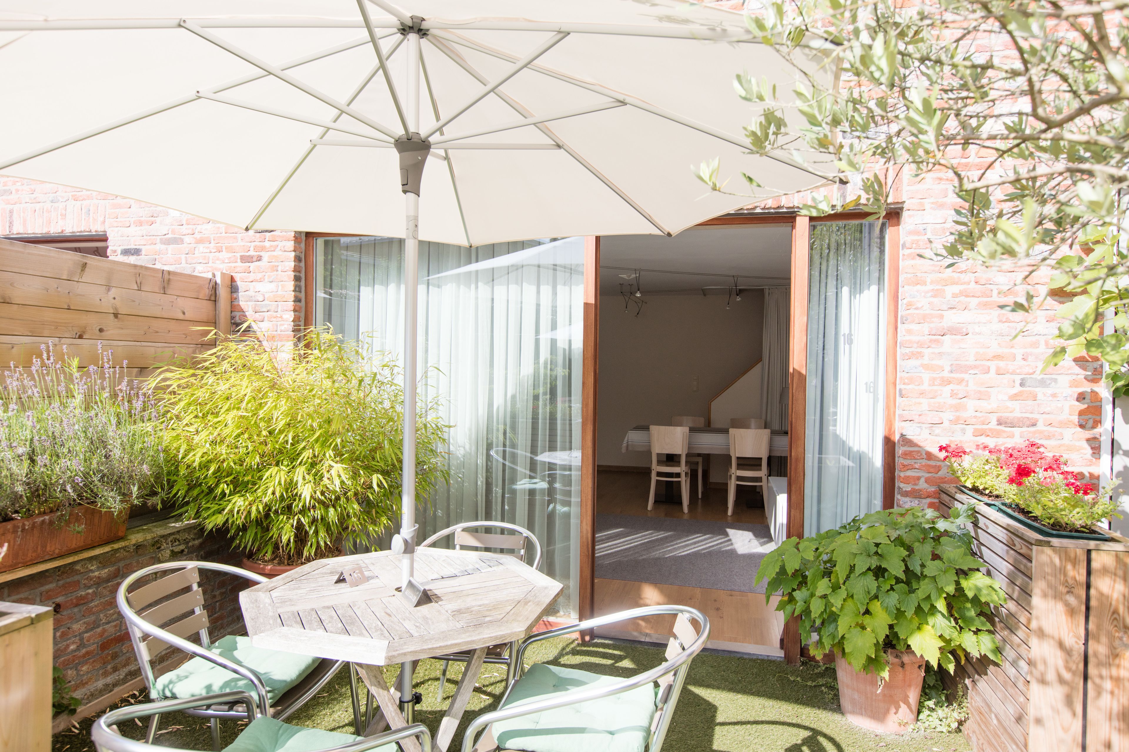 An outdoor patio with a wooden table and chairs, a large umbrella, and potted plants.