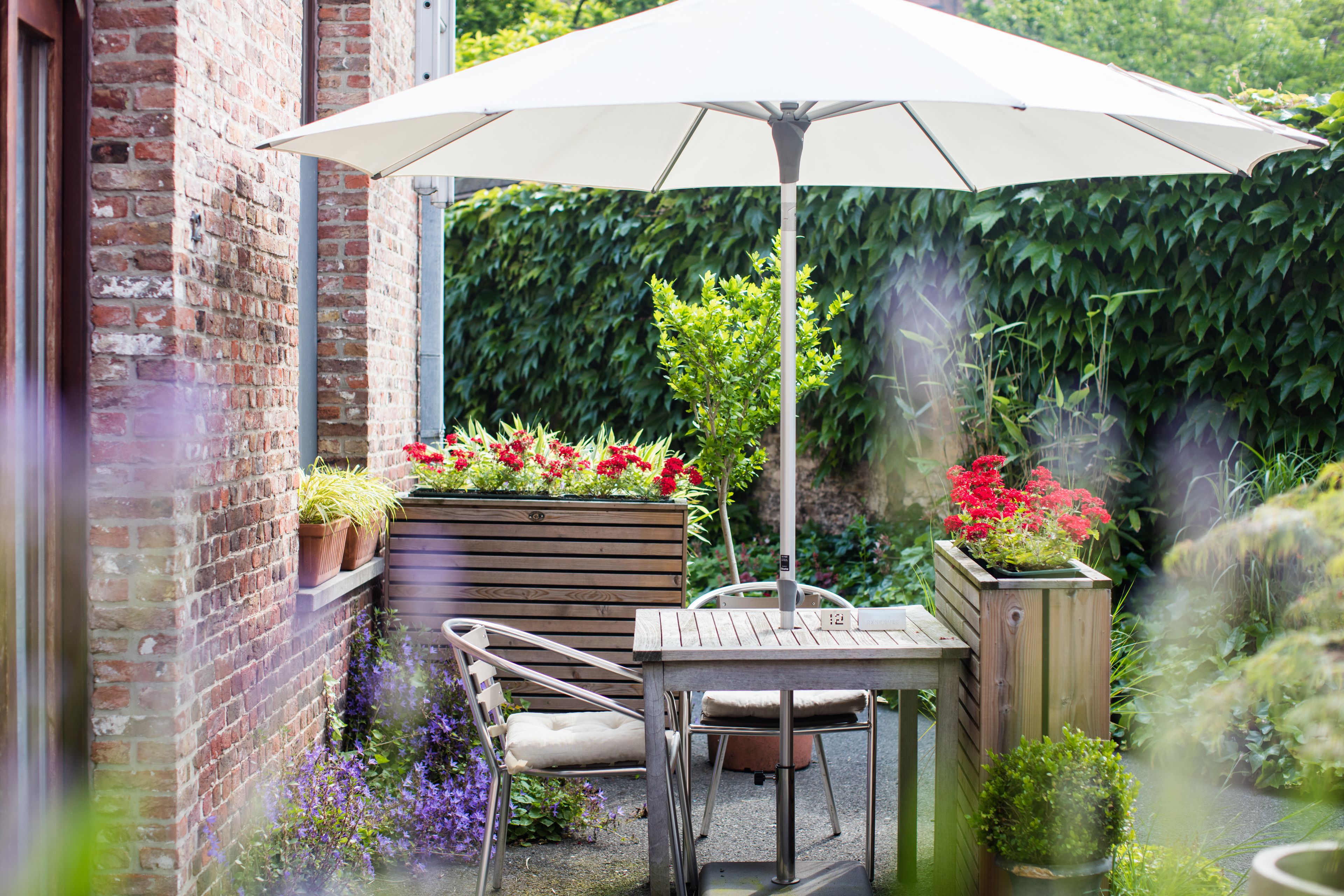 A patio with a table and chairs, a white umbrella, and potted plants.