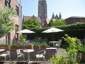 An outdoor patio with tables and chairs, surrounded by potted plants and flowers. - Bonobo Apartments (Bruges)