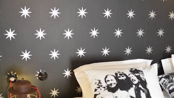 A bedroom with a star-patterned wall, a bed with white and black pillows, a blue stool, and a hanging light fixture.