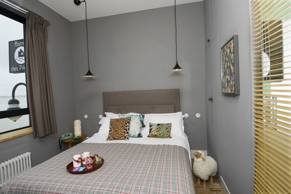 Een slaapkamer met een bed, nachtkastje, lamp en een raam met zonwering.