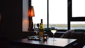 A table with a wine bottle, two glasses, a candle, and a lamp by a window with a view.