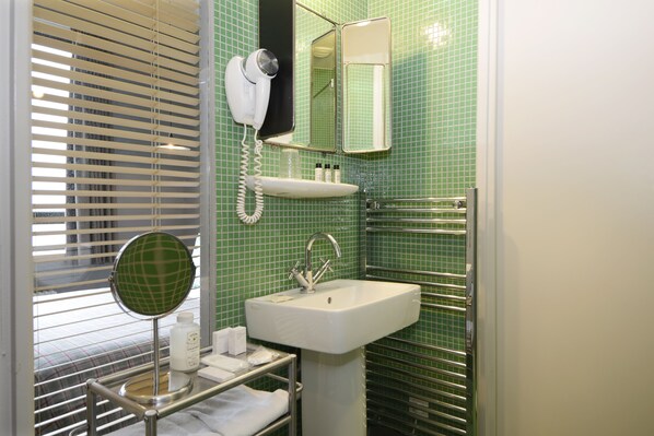 A bathroom with a green tiled wall, a white sink, a mirror, a hairdryer, and a towel rack. - Hôtel Les Pilotes (Saint-Valery-sur-Somme)