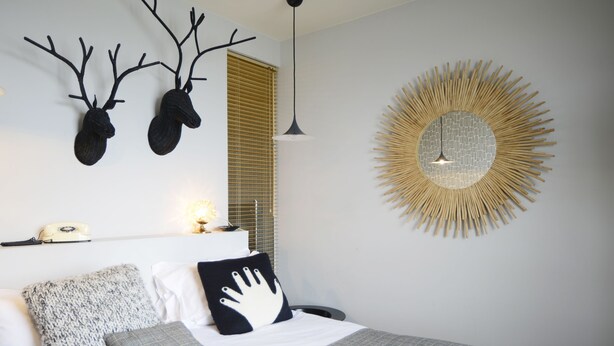 A neatly arranged bedroom with a bed, pillows, a book, a wall-mounted mirror, and a decorative wall piece.