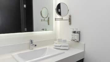 A modern bathroom with a white sink, two mirrors, and toiletries on the wall.