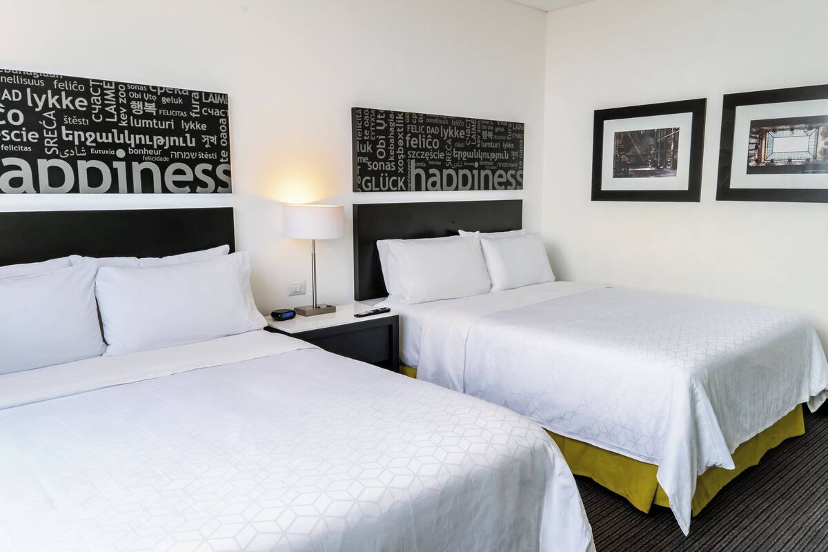 A hotel room with two beds, a nightstand, a lamp, and two framed pictures on the wall.
