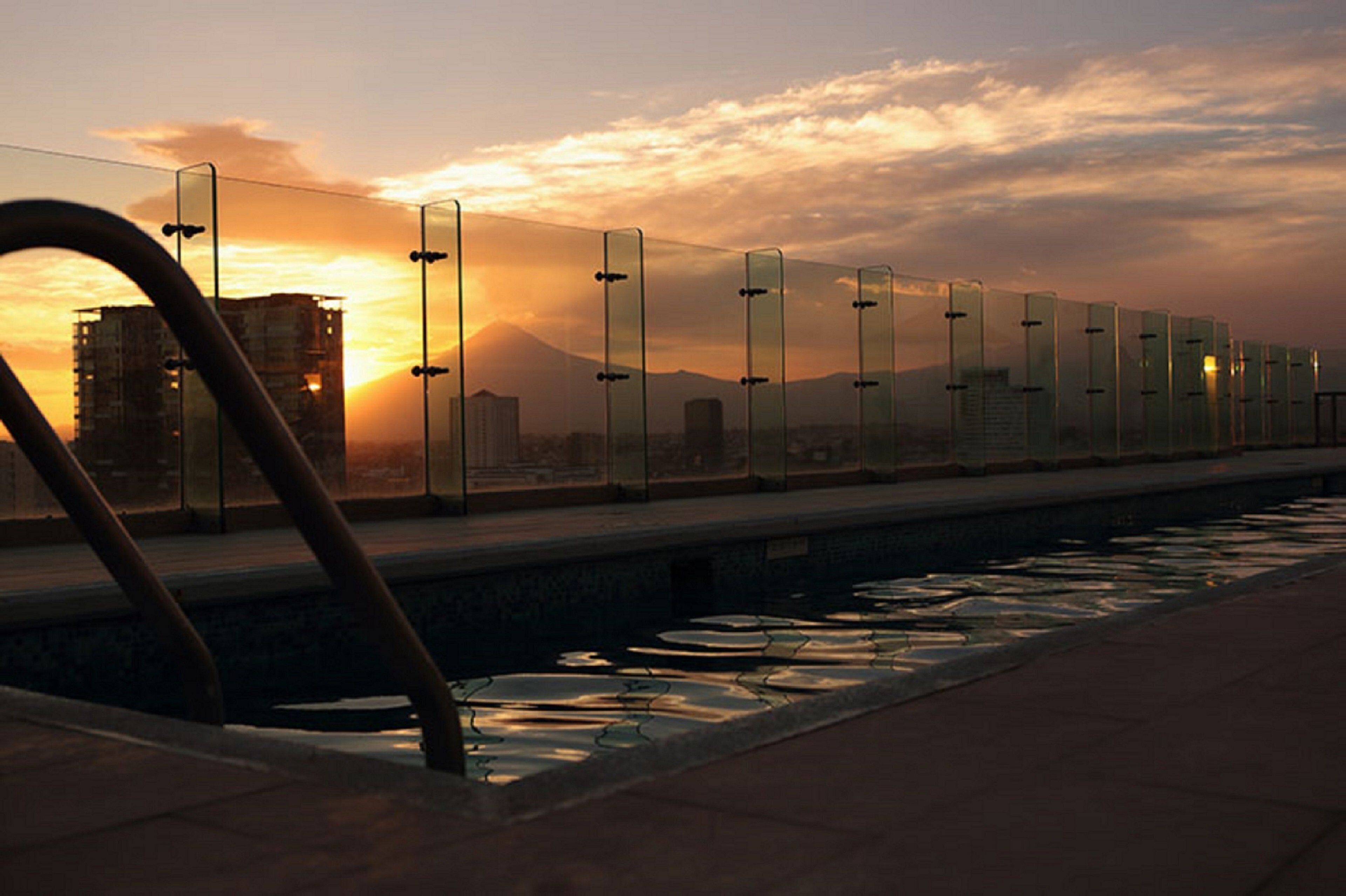 A sunset view with a glass railing overlooking a cityscape.