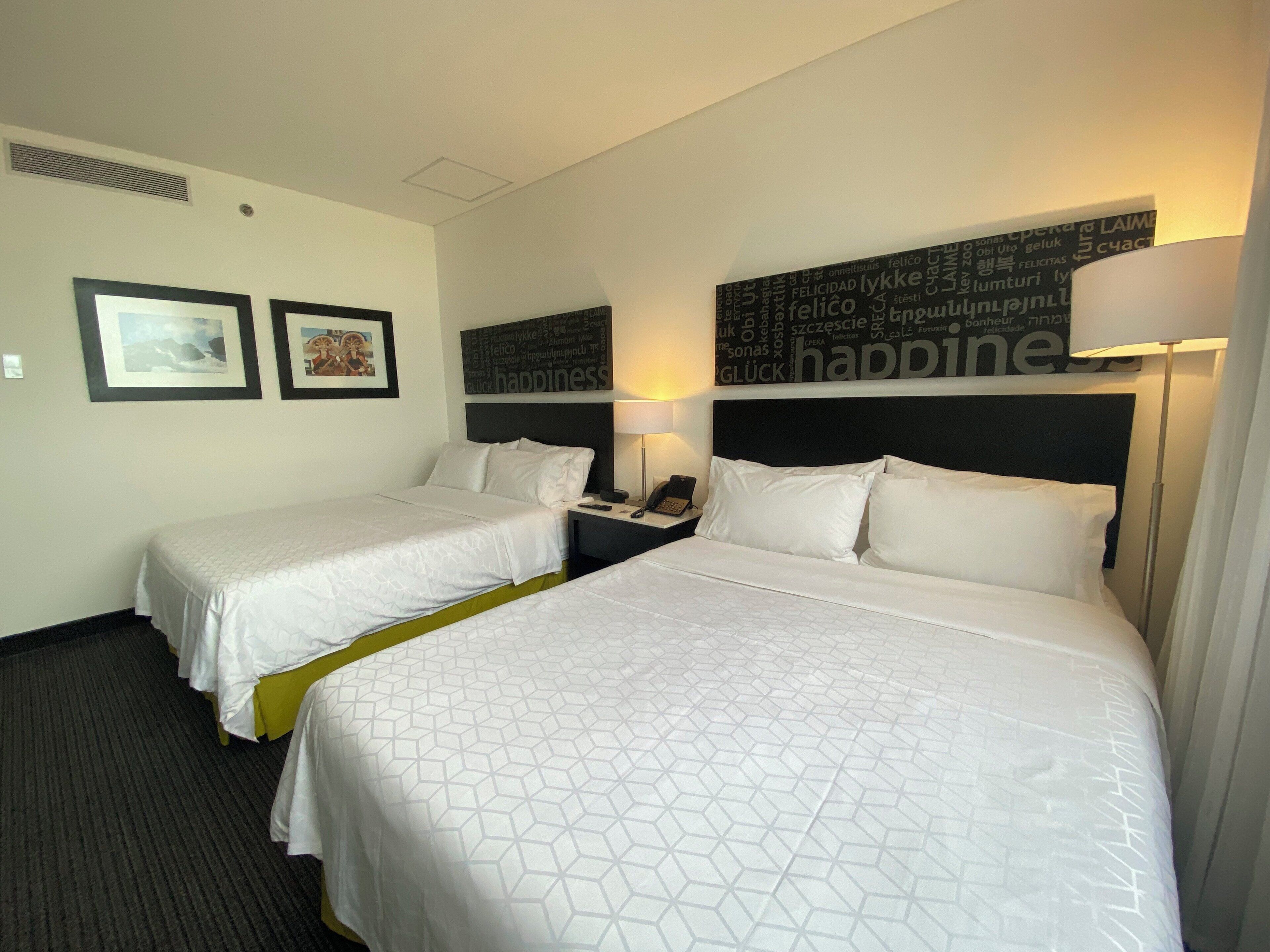 Habitación de hotel con dos camas, una mesita de noche con lámpara y decoración en la pared.