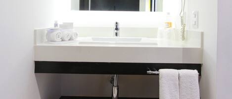Un baño moderno con un lavamanos blanco, un espejo, un secador de pelo y un tendedero para toallas.