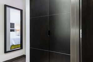Una habitación de hotel moderna con un espejo grande, una cama con sábanas blancas y un armario de color oscuro.